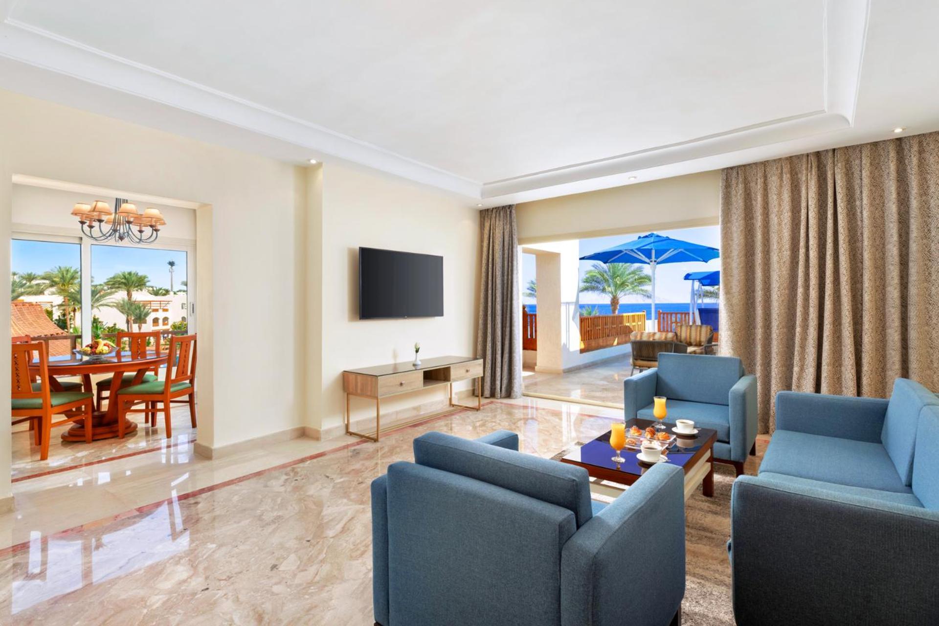 Pickalbatros Royal Grand Sharm - Adults Friendly 16 Years Plus Sharm El Sheikk Exterior foto The photo shows a modern and spacious living area. There are several blue chairs arranged around a coffee table, which holds some refreshments. A large flat-screen TV is mounted on the wall, and there are sliding glass doors that open to an outdoor a