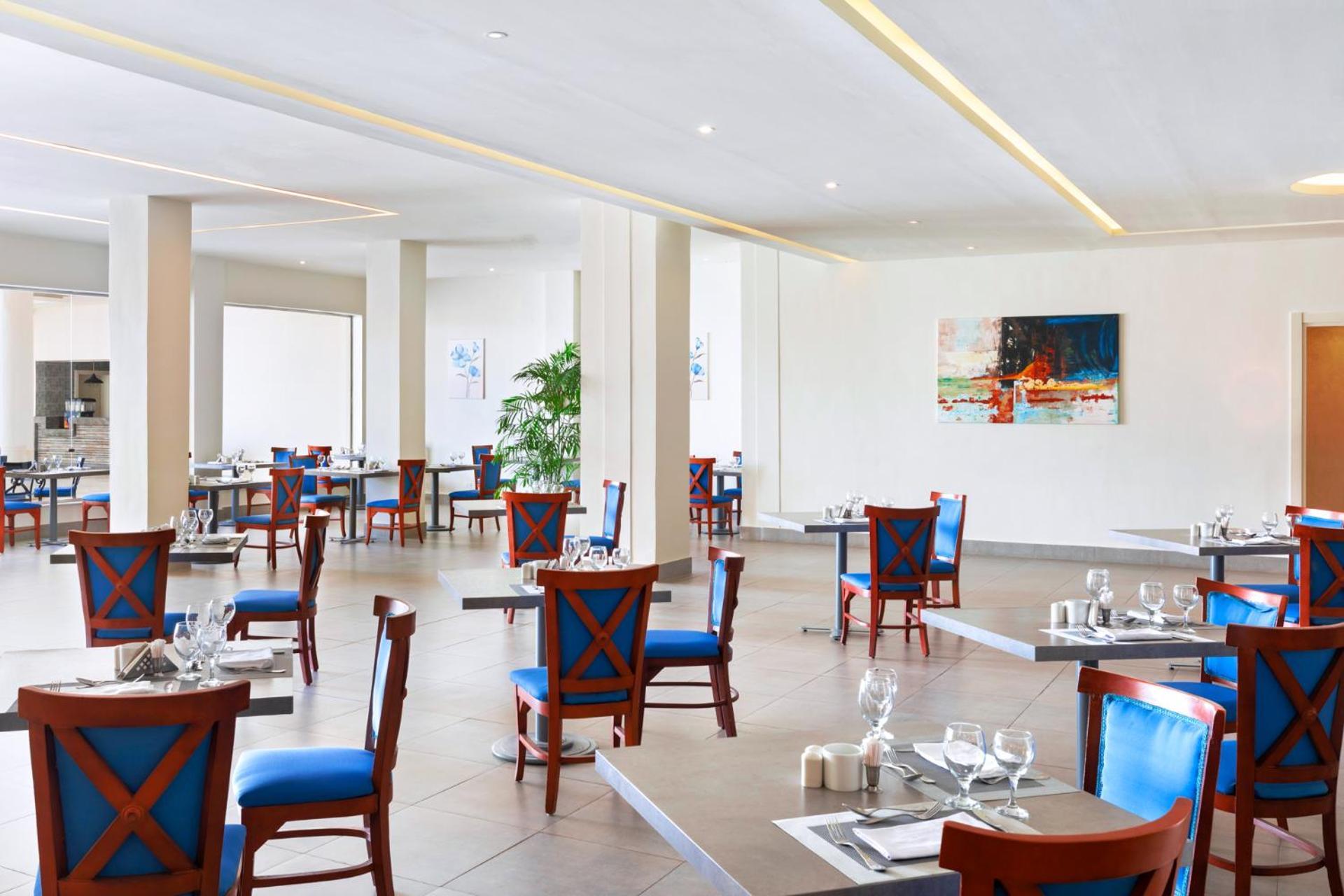 Pickalbatros Royal Grand Sharm - Adults Friendly 16 Years Plus Sharm El Sheikk Exterior foto The photo shows an interior of a restaurant featuring a modern and spacious design. The floors are tiled, and the walls are painted in neutral tones. The seating consists of wooden chairs with blue cushions arranged around tables, which are set with 