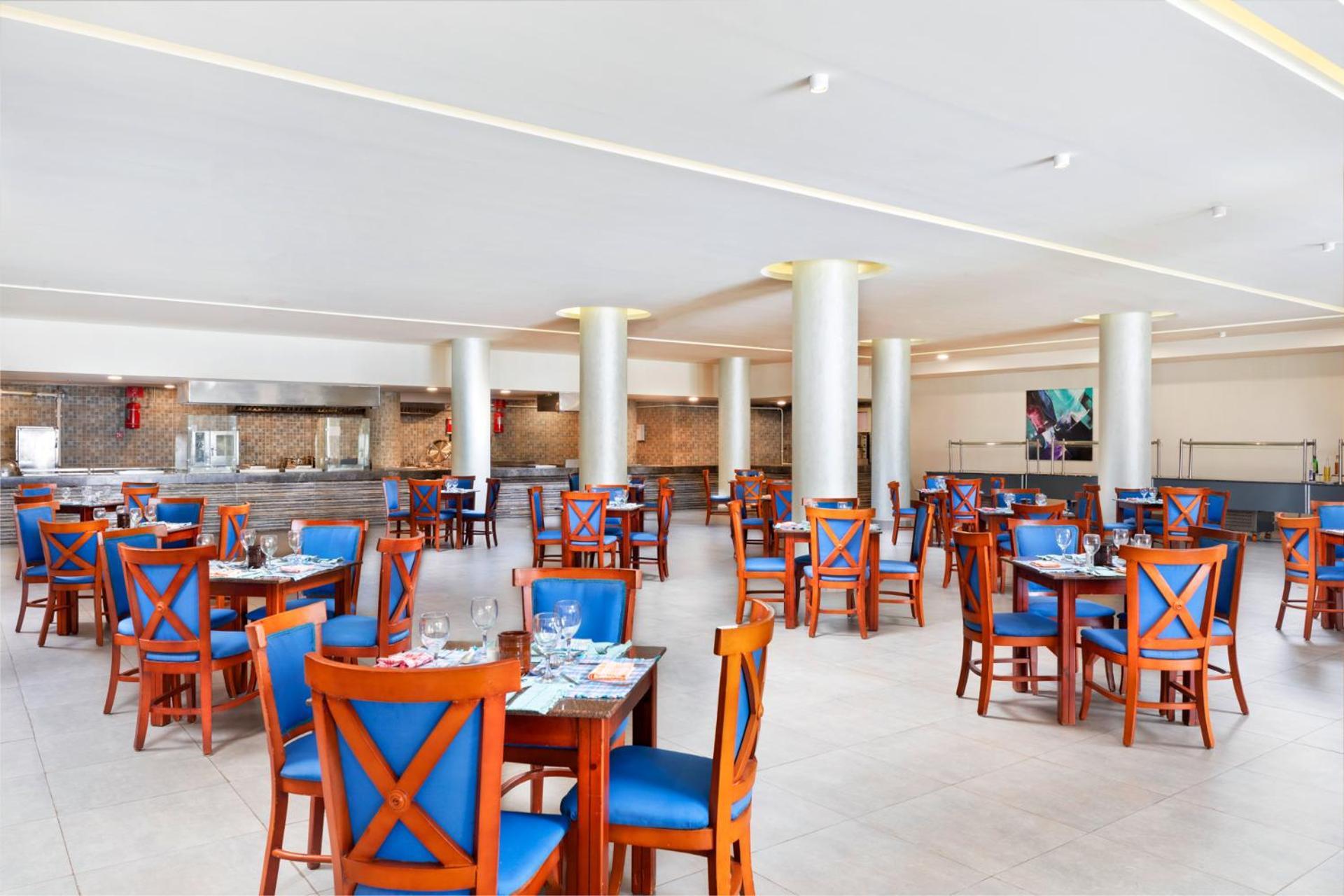 Pickalbatros Royal Grand Sharm - Adults Friendly 16 Years Plus Sharm El Sheikk Exterior foto The photo depicts a spacious dining area in a restaurant. The room features several wooden tables, each with blue chairs. The chairs have a unique design with prominent X-shaped backs. The flooring is light-colored tile, and the walls are painted in 