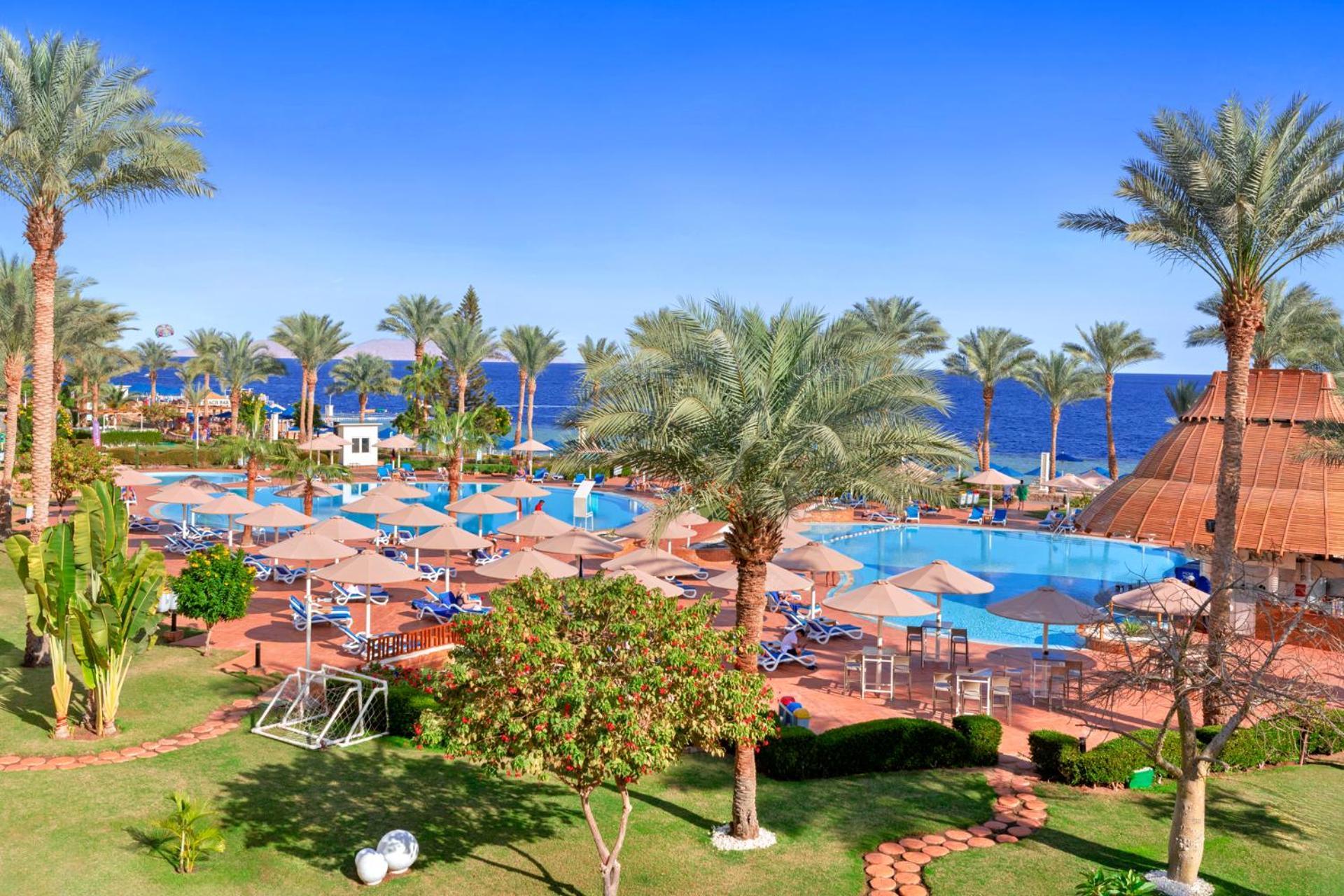Pickalbatros Royal Grand Sharm - Adults Friendly 16 Years Plus Sharm El Sheikk Exterior foto The photo depicts a tropical resort setting by the sea. It features a large swimming pool surrounded by sun loungers and umbrellas. Lush palm trees are scattered throughout the area, providing shade and a picturesque backdrop. In the background, you 