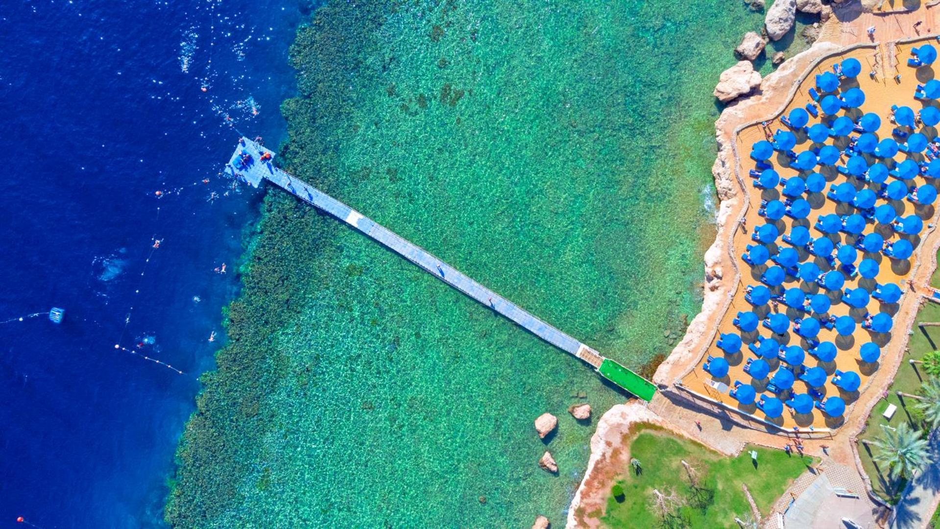 Pickalbatros Royal Grand Sharm - Adults Friendly 16 Years Plus Sharm El Sheikk Exterior foto The photo shows an aerial view of a coastal area featuring a long wooden pier extending into clear turquoise water. On one side of the pier, there appears to be a beach with umbrellas or sunbeds arranged neatly. The water is vibrant and visually invi