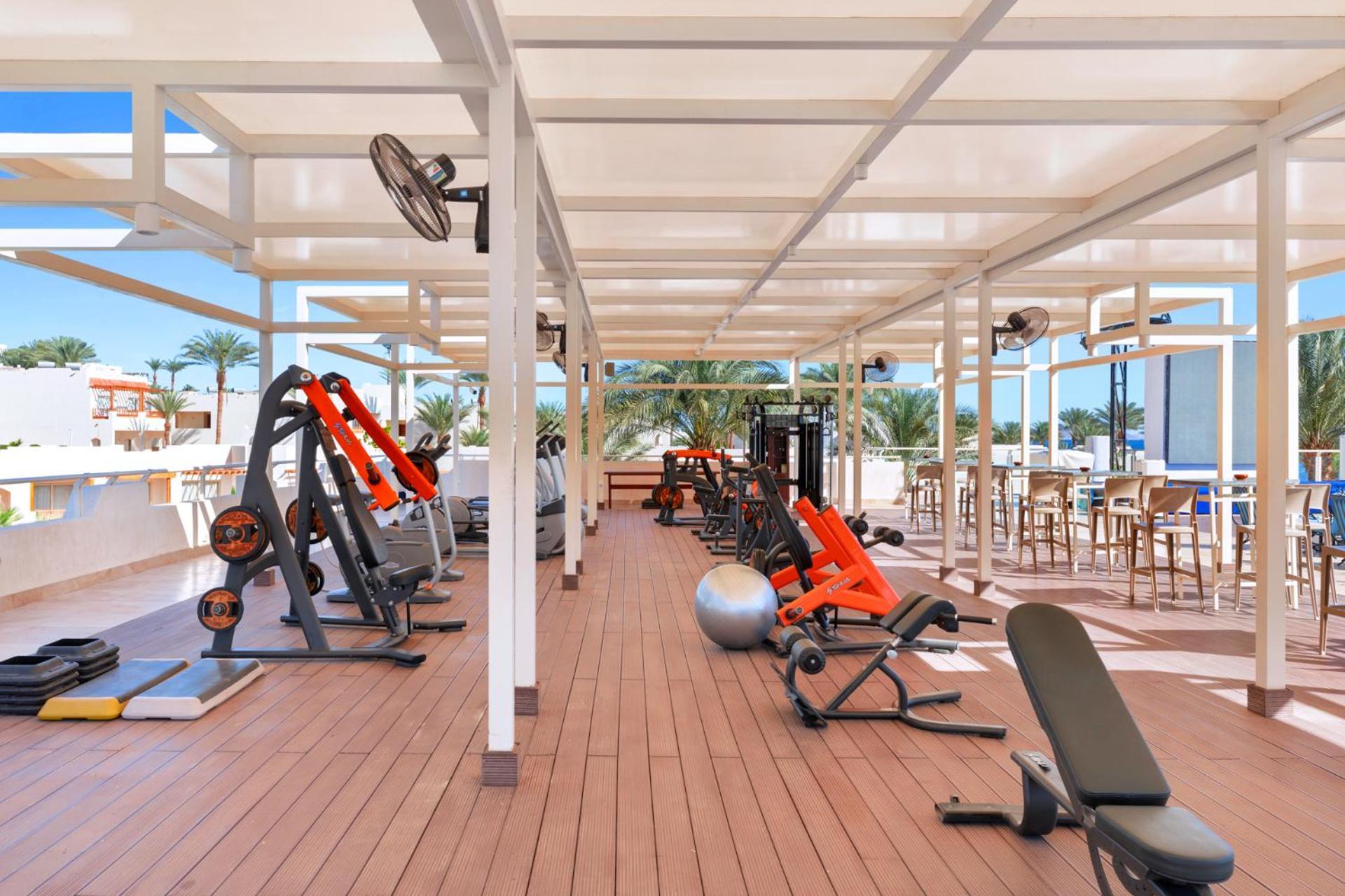 Pickalbatros Royal Grand Sharm - Adults Friendly 16 Years Plus Sharm El Sheikk Exterior foto The photo depicts a gym area located outdoors or in a covered terrace, featuring various fitness equipment. There are several weight machines and benches, as well as some free weights. Large fans are installed for ventilation, and the space is design